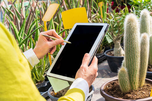 Eine Gärtnerin benutzt ein modernes Tablet, während sie Pflanzen zählt und in einem Gartencenter arbeitet - ADSF24442