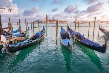 Traditional gondolas moored on rippling water surface on background of city and sundown sky in Venice - ADSF24474