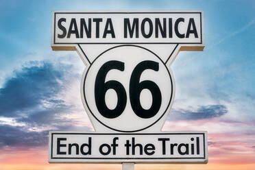 Niedriger Winkel des Schildes mit der Aufschrift Santa Monica 66 End of the Trail vor dem Hintergrund des farbenfrohen Himmels bei Sonnenuntergang - ADSF24476