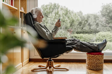 Senior man using smart phone while listening music through headphones at home - AFVF08762