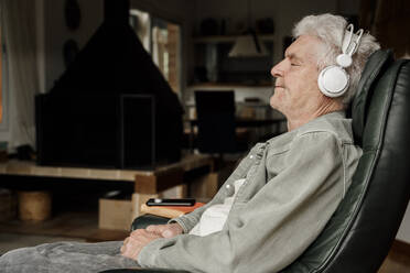 Senior man wearing headphones resting at home - AFVF08765