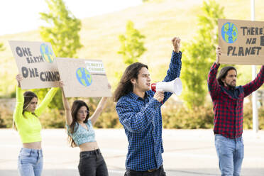Junger männlicher Aktivist protestiert gegen den Klimawandel mit männlichen und weiblichen Demonstranten auf dem Fußweg - JCCMF02434