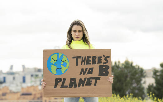 Frau mit Plakat zum Klimawandel vor dem Himmel stehend - JCCMF02451