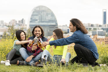 Fröhliche männliche und weibliche Freunde stoßen mit Bierflaschen auf einem Feld an - JCCMF02464