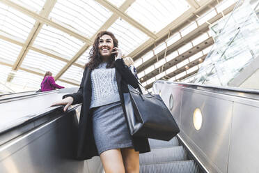 Lächelnde Geschäftsfrau, die sich auf einer Rolltreppe nach unten bewegt - WPEF04454