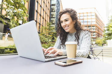 Smiling businesswoman using laptop at cafe in city - WPEF04457