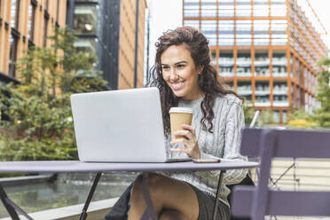 Happy businesswoman using laptop in city - WPEF04459