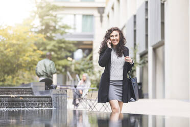 Happy businesswoman using mobile phone in city - WPEF04465