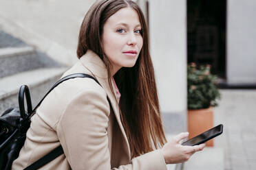 Junge Frau mit Rucksack starrt und hält Smartphone - EBBF03511