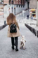 Brown hair woman walking with dog on footpath - EBBF03516