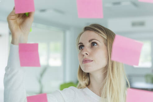 Businesswoman writing on adhesive notes on glass in office - MCVF00833