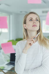 Thoughtful businesswoman looking at adhesive note at office - MCVF00834