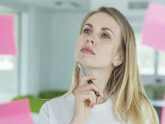 Blonde Unternehmerin beim Brainstorming mit Blick auf einen Klebezettel im Büro - MCVF00835