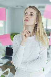 Thoughtful female entrepreneur looking at adhesive note in office - MCVF00836