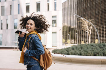 Young curly hair woman talking on mobile phone in city - JCZF00704