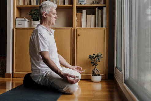 Mann übt Yoga, während er zu Hause im Lotussitz sitzt - AFVF08775