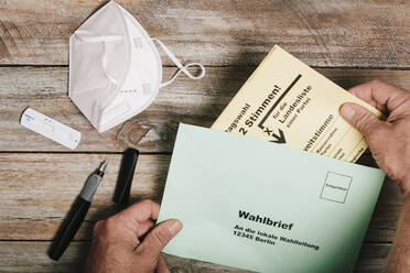 Hand, die den Stimmzettel für die Bundestagswahl in einen Umschlag auf einem Tisch mit Schutzmaske und Korona-Schnelltest steckt - MMFF01298