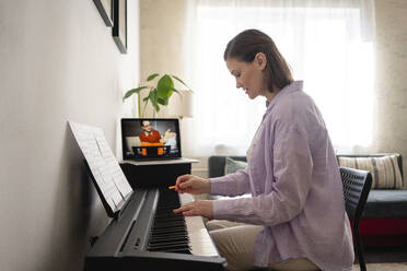 Woman learning piano during online tutorial through laptop at home - VPIF03998