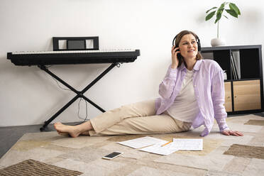Mittlere erwachsene Frau mit Kopfhörern, die zu Hause auf einem Teppich sitzt - VPIF04004