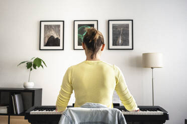Mid adult woman learning piano in front of picture frame at home - VPIF04013