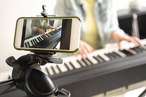 Filming on mobile phone while woman playing piano at home - VPIF04022