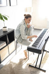 Mid adult woman practicing piano while sitting in living room - VPIF04025