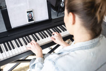 Mid adult woman on video call while practicing piano at home - VPIF04026