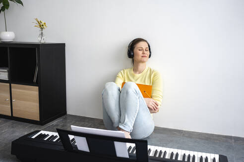 Schöne Frau mit Kopfhörern hört Musik, während sie sich zu Hause an die Wand lehnt - VPIF04029
