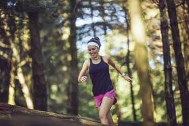 Smiling sportswoman running in forest - MTBF00989