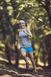 Smiling young sportswoman running in forest - MTBF00996