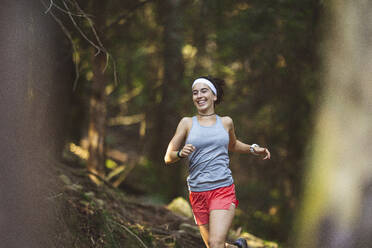 Lächelnde Frau in Sportkleidung beim Laufen im Wald - MTBF00998
