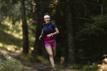 Happy young female sportsperson running in forest - MTBF01004