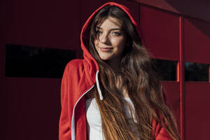 Smiling teenage girl wearing red hooded jacket on sunny day - JRVF00594