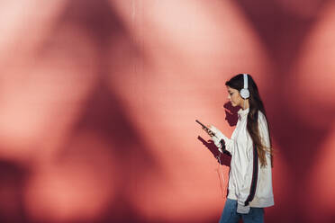 Teenager-Mädchen, das ein Mobiltelefon benutzt, während es an einer roten Wand vorbeiläuft - JRVF00602
