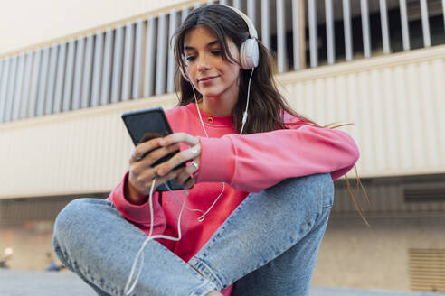 Hübsches Teenager-Mädchen trägt Kopfhörer, während sie ihr Smartphone benutzt - JRVF00603