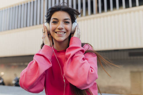 Lächelndes Teenager-Mädchen mit Kopfhörern beim Musikhören - JRVF00604