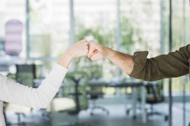 Male and female colleagues greeting with fist bumps in office - MCVF00855