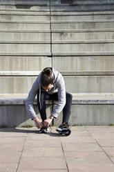 Man tying shoelace while sitting on steps - VEGF04454