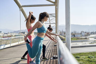 Männliche und weibliche Freunde machen Aufwärmübungen auf einer Brücke - VEGF04470