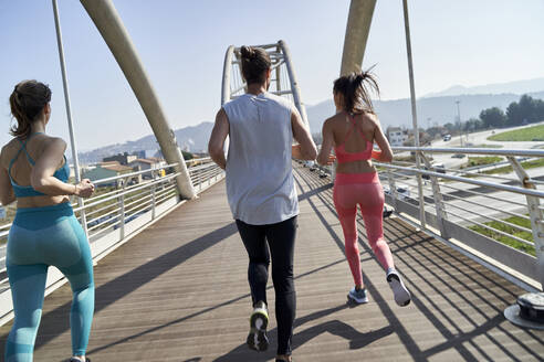 Männliche und weibliche Freunde joggen auf einer Brücke an einem sonnigen Tag - VEGF04472