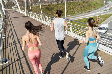Multi ethnic male and female friends running on bridge during sunny day - VEGF04474