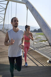 Männlicher und weiblicher Sportler beim Joggen auf einer Brücke - VEGF04475