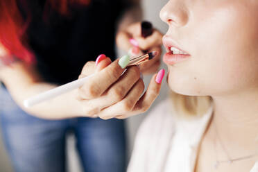 Female make-up artist applying lipstick to model in studio - MRRF01103