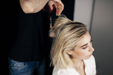 Female hairstylist doing hairstyle of blond model in studio - MRRF01120
