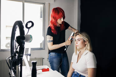 Weiblicher Friseur mit Glätteisen auf dem Haar des Modells vor Ringlicht im Studio - MRRF01121