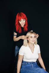 Female stylist doing hairstyle of smiling model in studio - MRRF01137