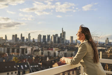Geschäftsfrau mit Blick auf die Stadtlandschaft, während sie auf dem Dach steht - AKLF00160