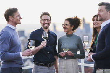 Lächelnde männliche und weibliche Unternehmer stehen mit Weingläsern auf der Terrasse eines Gebäudes - AKLF00182
