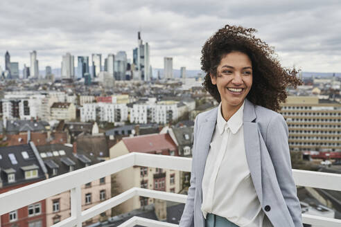 Smiling female entrepreneur on rooftop in city - AKLF00184