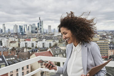 Happy mid adult businesswoman using mobile phone on rooftop - AKLF00186